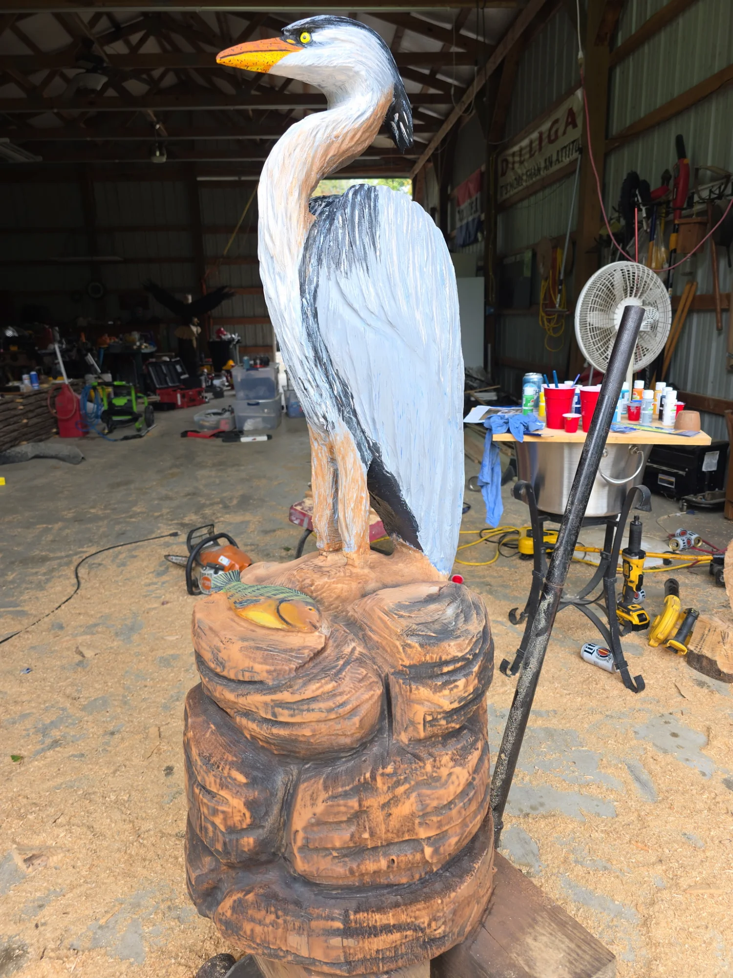 Blue Heron chainsaw carving standing on rocks with a fish, painted in natural colors