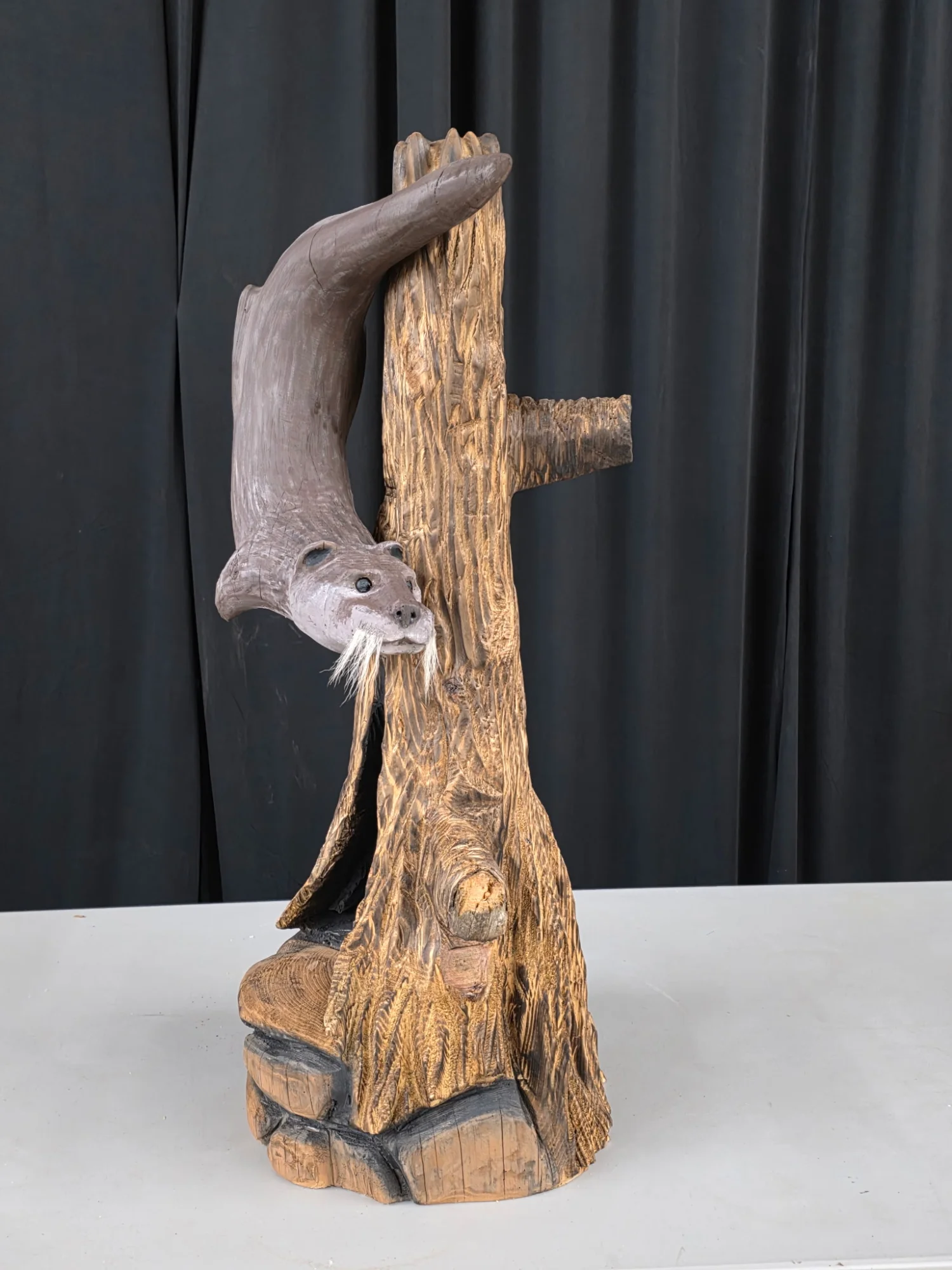 River Otter chainsaw carving climbing a log with carved rocks at the base